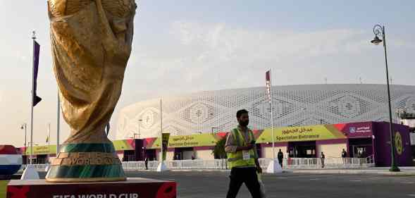 A stadium worker walks past a large statue of the World Cup in Qatar