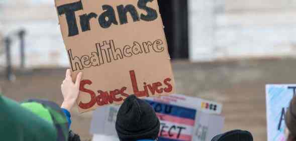 A trans rights protester holds a sign that reads: "Trans healthcare saves lives."