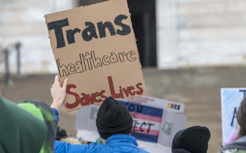 A trans rights protester holds a sign that reads: "Trans healthcare saves lives."