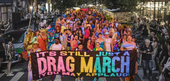 A photo of pro-drag march with people at the front of the crowd holding a banner with the slogan "It's still just a drag march, you may applaud".