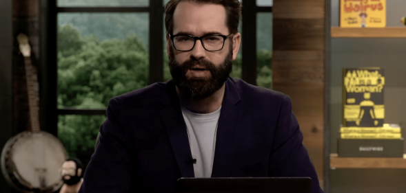 A screenshot of right-wing columnist and blogger Matt Walsh wearing glasses, black suit jacket over a white T-shirt talking on his YouTube show