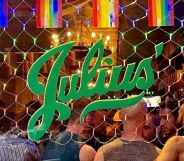 A photo showing an exterior shot of New York gay bar Julius' - showing Pride flags across the top, the green Julius' logo and people on the inside of the club