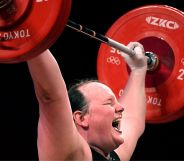 A photo of New Zealand trans athlete weightlifter Laurel Hubbard showing signs of physical strain as she lifts a dumbbell weight over her head during the Olympics.