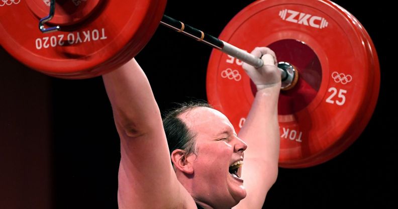 A photo of New Zealand trans athlete weightlifter Laurel Hubbard showing signs of physical strain as she lifts a dumbbell weight over her head during the Olympics.