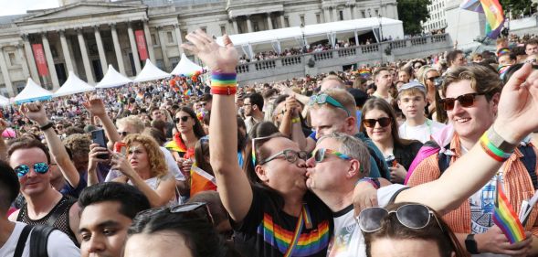 A crowded group sees two people kiss each other while raising their hands during the Pride in London parade