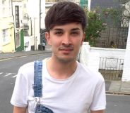 A photo of one of the Manchester Arena bombing victims, Martyn Hett, wearing a white t-shirt and dungerees with one strap, smiling outside a street corner.