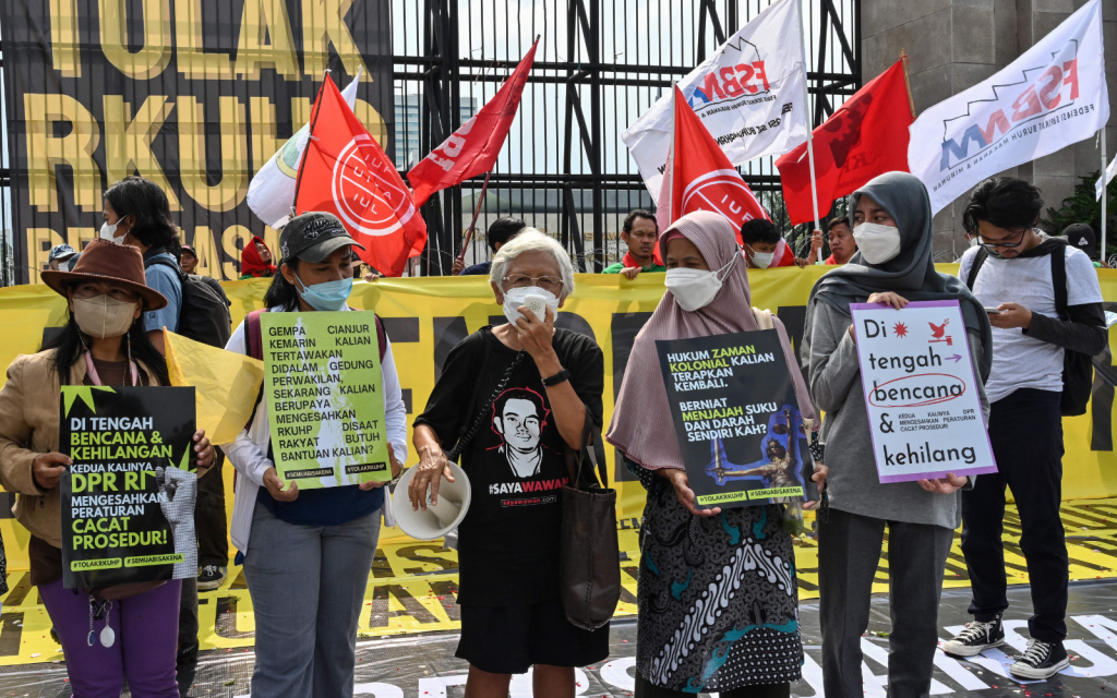 Indonesian protestors hold signs while surrounded by banners protesting the revised criminal code