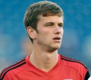 Collin Martin, wearing a red shirt, stands on the pitch of a football stadium.