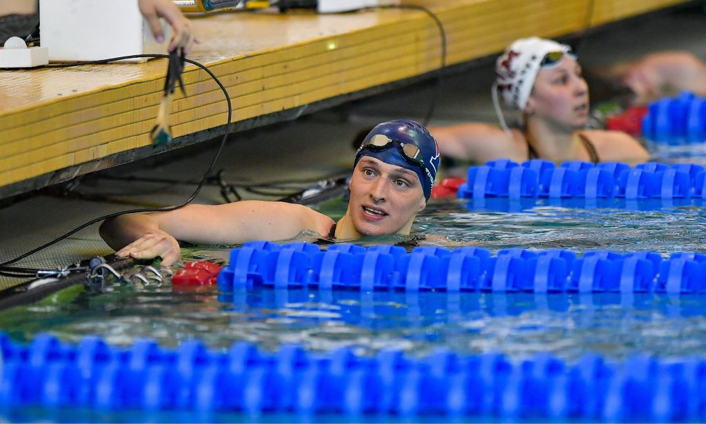 Lia Thomas waits on the side of a swimming pool, neck deep, after having swam in a race.