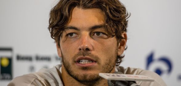 Taylor Fritz, wearing a white tee, speaks during a press conference into a small microphone.