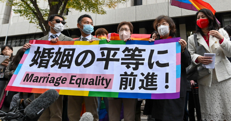 Plaintiffs holding up a rainbow-themed banner supporting marriage equality as a rainbow flag waves in the background.