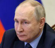 Vladimir Putin stares at someone off camera while sitting in front of a Russian flag after signing an extended LGBTQ+ 'propaganda' bill into law