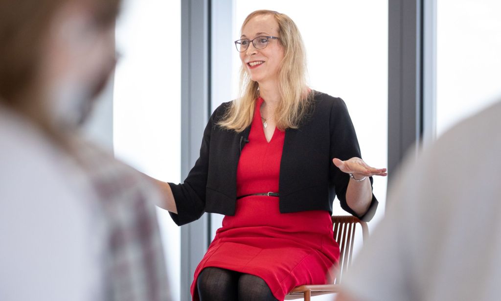 Trans ambassador Katie Neeves wears a red dress and black jacket on top as she speaks to people about her experiences and the joy of being openly trans