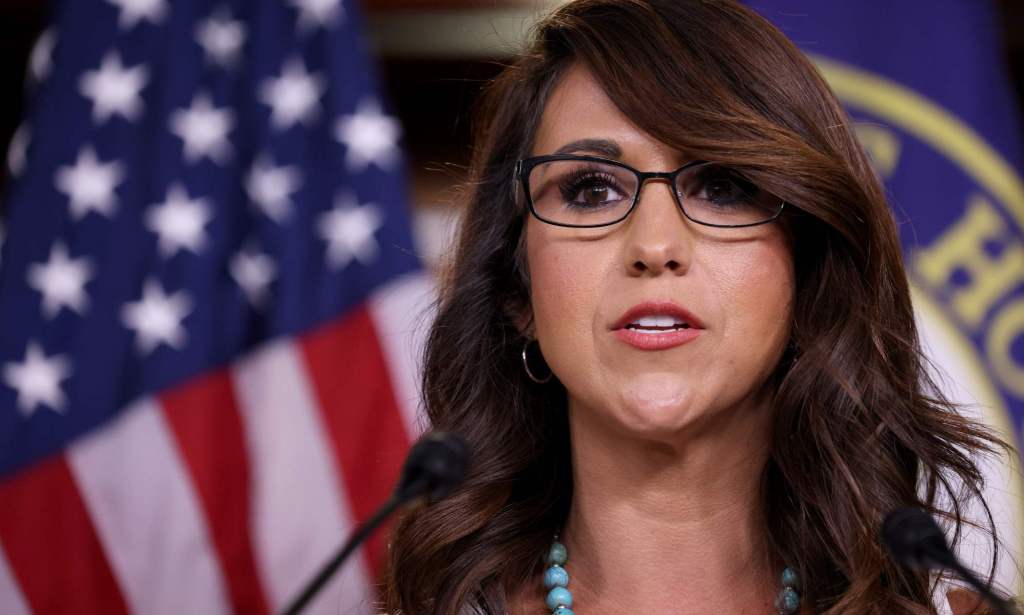 Lauren Boebert speaks into a microphone with a red, white and blue US flag in the background