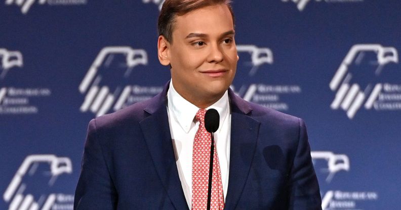 George Santos wears a suit and tie while speaking into a microphone at a conference