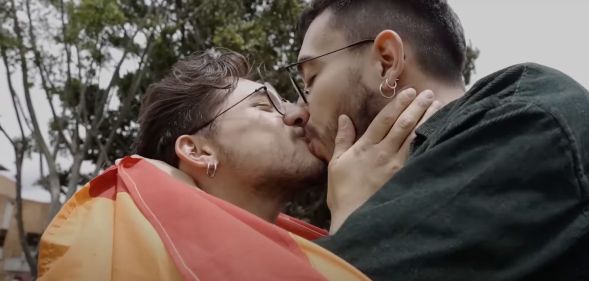 A person wearing a rainbow LGBTQ+ pride flag leans in to kiss another person