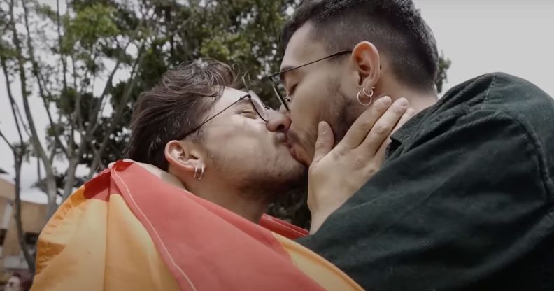 A person wearing a rainbow LGBTQ+ pride flag leans in to kiss another person