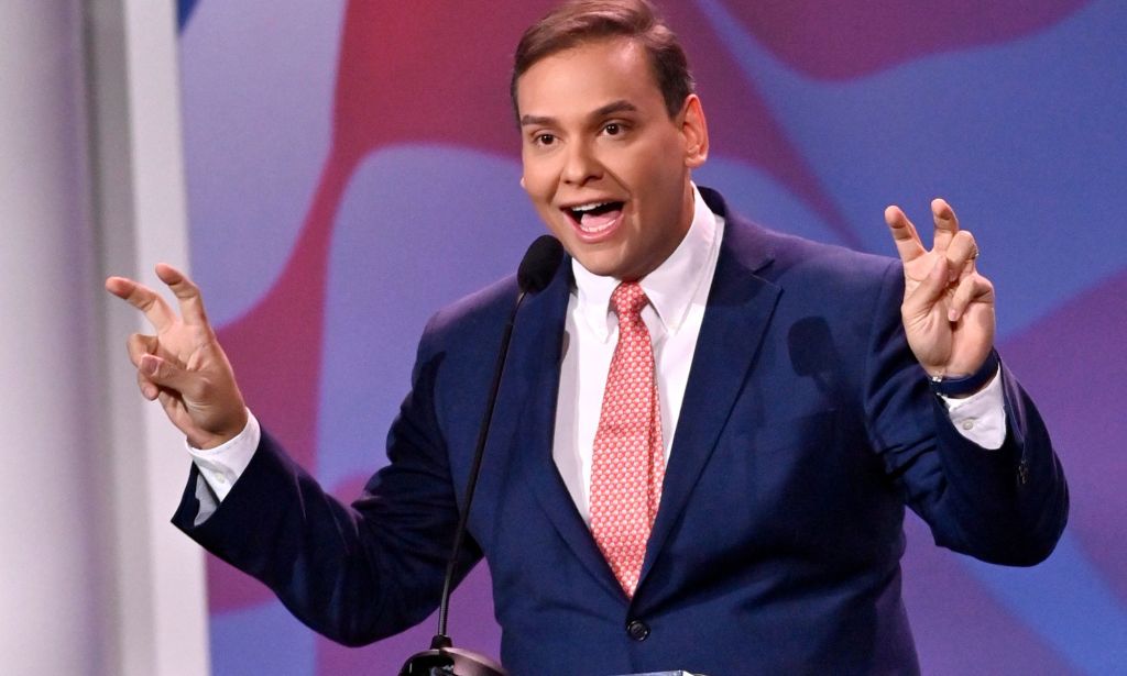 Republican politician George Santos gestures with his hands near his face while speaking at a podium