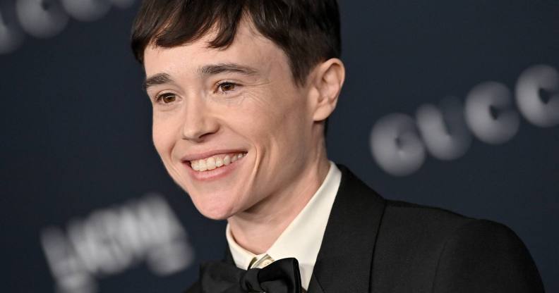 Elliot Page smiles at the camera while wearing a black and white tuxedo