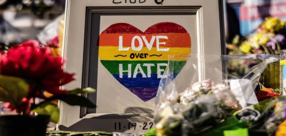 Flowers and a picture of a heart drawn in Pride rainbow colours with the message "Love over Hate" are placed outside Club Q