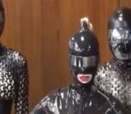 A screengrab from Twitter shows three people dressed in black latex, head-to-toe body suits standing in front of a wall