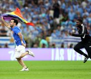 A photo of a pitch invader wearing a shirt reading "Save Ukraine" as he holds a rainbow flag during the FIFA World Cup Qatar 2022.