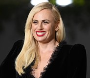 Photo of actor Rebel Wilson dressed in a black dress smiles for the cameras at a press event