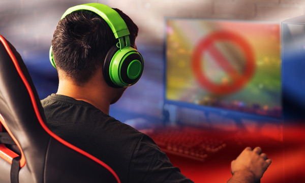 A person wearing green over-head earphones plays on a desktop computer, with the monitor containing a crossed-out LGBT symbol.