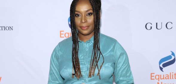 Chimamanda Ngozi Adichie wears a blue dress as she holds a copy of a book.