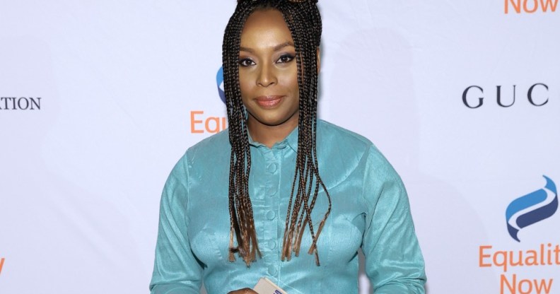 Chimamanda Ngozi Adichie wears a blue dress as she holds a copy of a book.