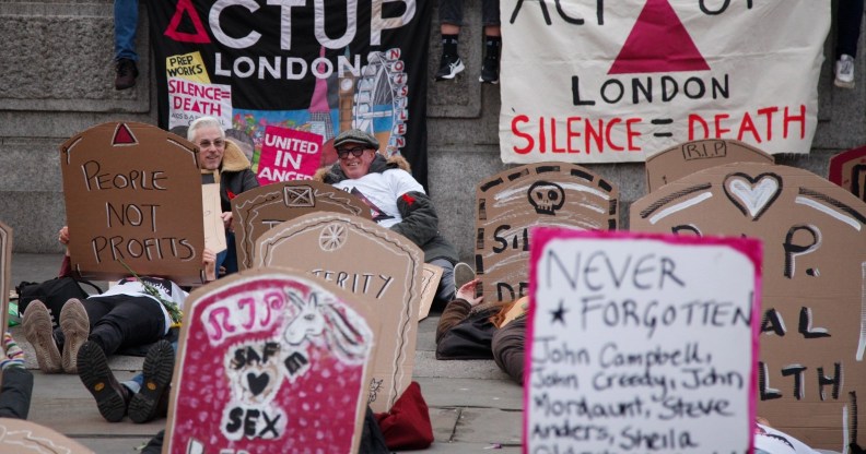 Activists lie down in Trafalgar Square holding cardboard gravestones with messages saying "cuts = coffins", and "queer people are dying" on World AIDS Day