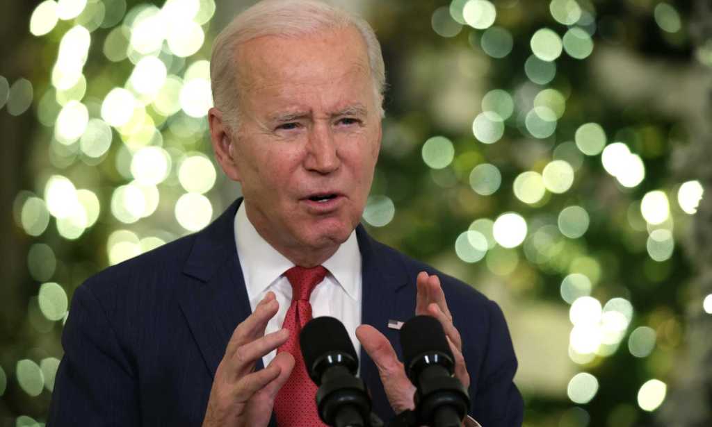 Joe Biden speaking into a microphone, there are Christmas trees in the background