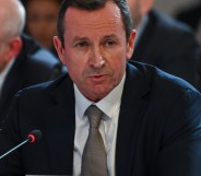 Western Australia Premier Mark McGowan dressed in a dark suit, white shirt and grey tie sits in front of a microphone