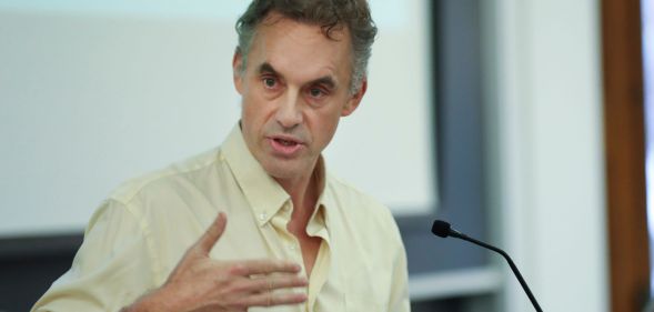 Jordan Peterson speaks during a lecture while wearing a slightly yellow t shirt
