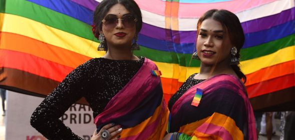 Members of the LGBTQ+ community in India stand infront of a Pride rainbow flag.