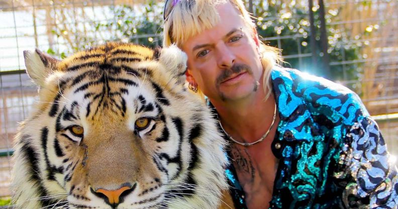 Joe Exotic hugs a tiger while wearing a blue and white shiny jacket.