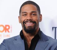 A photo showing professional wrestler Fred Rosser wearing a light blue suit jacket and black shirt smiling to the camera while on the red carpet.