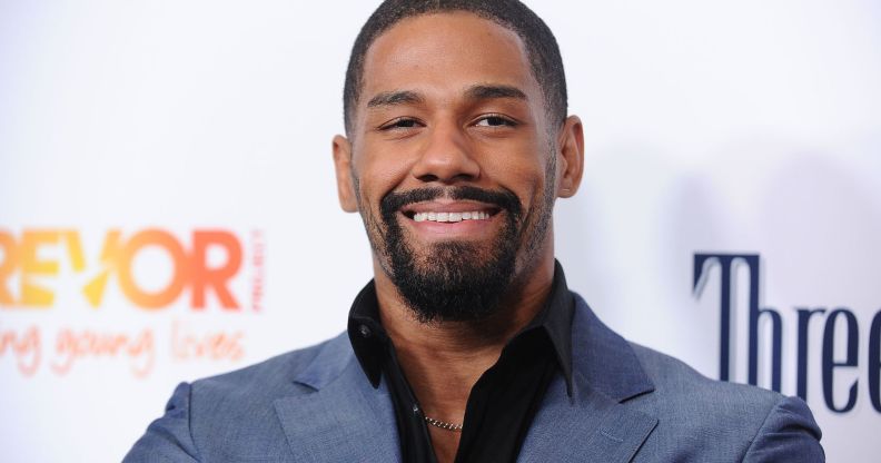 A photo showing professional wrestler Fred Rosser wearing a light blue suit jacket and black shirt smiling to the camera while on the red carpet.