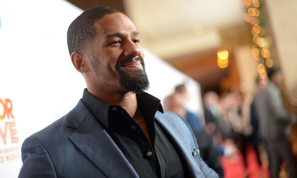 Fred Rosser smiles to members of the red carpet, wearing a silver blazer.