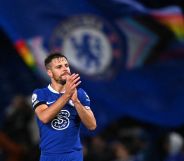 Chelsea player Cesar Azpilicueta claps during the end of a match while a Pride Chelsea flag waves in the background.