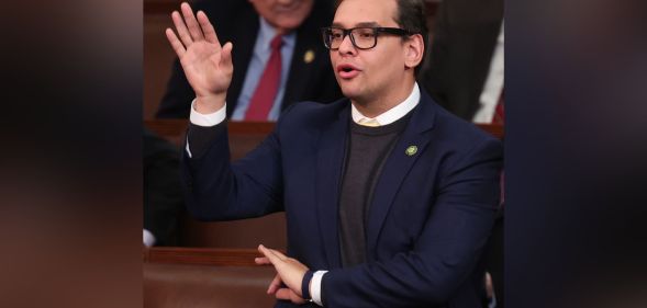 George Santos, wearing a suit, holds up his right hand to cast a vote on the US House floor while the other hand makes an 'OK' gesture