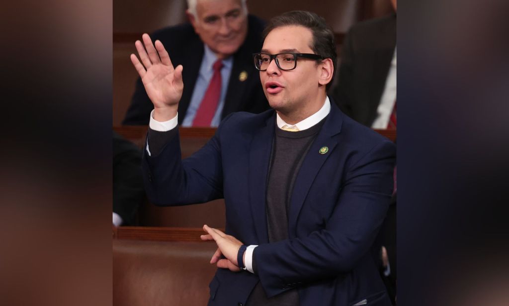 George Santos, wearing a suit, holds up his right hand to cast a vote on the US House floor while the other hand makes an 'OK' gesture