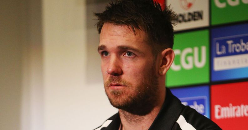 A photo shows Former Australian Football League (AFL) star Dane Swan wearing a black and white top sitting in a room with the names of football sponsors on the wall behind him