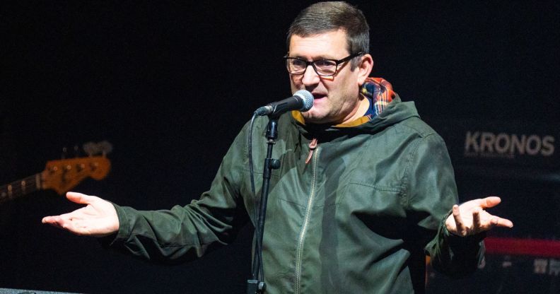 A photo shows singer-songwriter Paul Heaton wearing a green coat and standing behind a microphone on stage as he holds his hands up