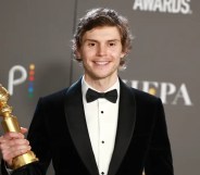 Evan Peters wearing a black suit jacket and bow tie holding his Golden Globe award and standing against a black background with the NBC logo on it