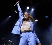 A photo of singer Fletcher wearing a purple suit performing on stage at London's 02 Forum with her hand in the air holding a microphone.