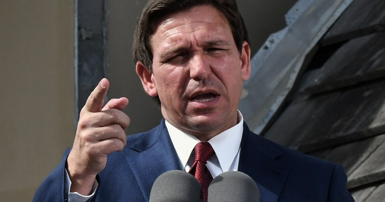 Florida governor Ron DeSantis wearing a navy suit, white shirt and red tie, stands in front of a microphone at a press conference