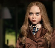 A still from the movie M3GAN shows the titular robotic doll wearing a silvery-brown coat as she stares out of a window. (Universal Pictures)