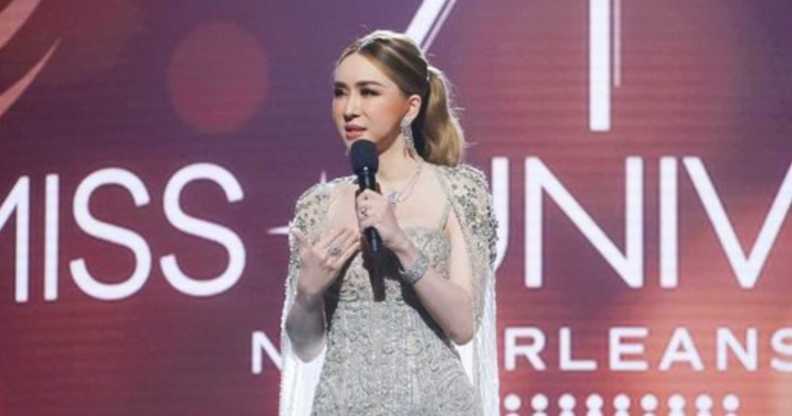 A still from the 71st Miss Universe pageant shows the franchise's owner, a trans woman called Jakkaphong "Anne" Jakrajutatip wearing a silver dress and holding a microphone standing on a stage with the "Miss Universe New Orleans" logo showing in the background