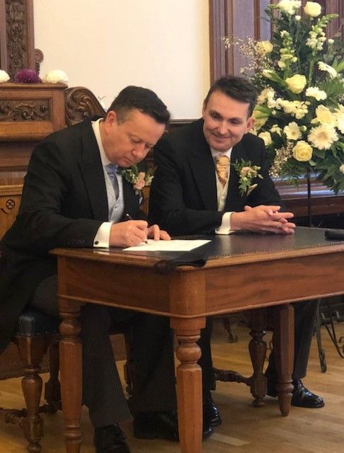 Paul and Alain on their wedding day. they are pictured signing the marriage register in a registry office.